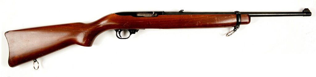 A Ruger 10/22 rifle with a wooden stock and metal barrel resting on a surface, showing its classic small‑caliber design, bolt action, and sling attachment points.